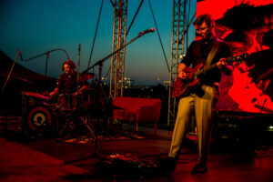 Zdjęcie z festiwalu, koncert na scenie, na zdjęciu gitarzysta i perkusista oświetleni na czerwono
