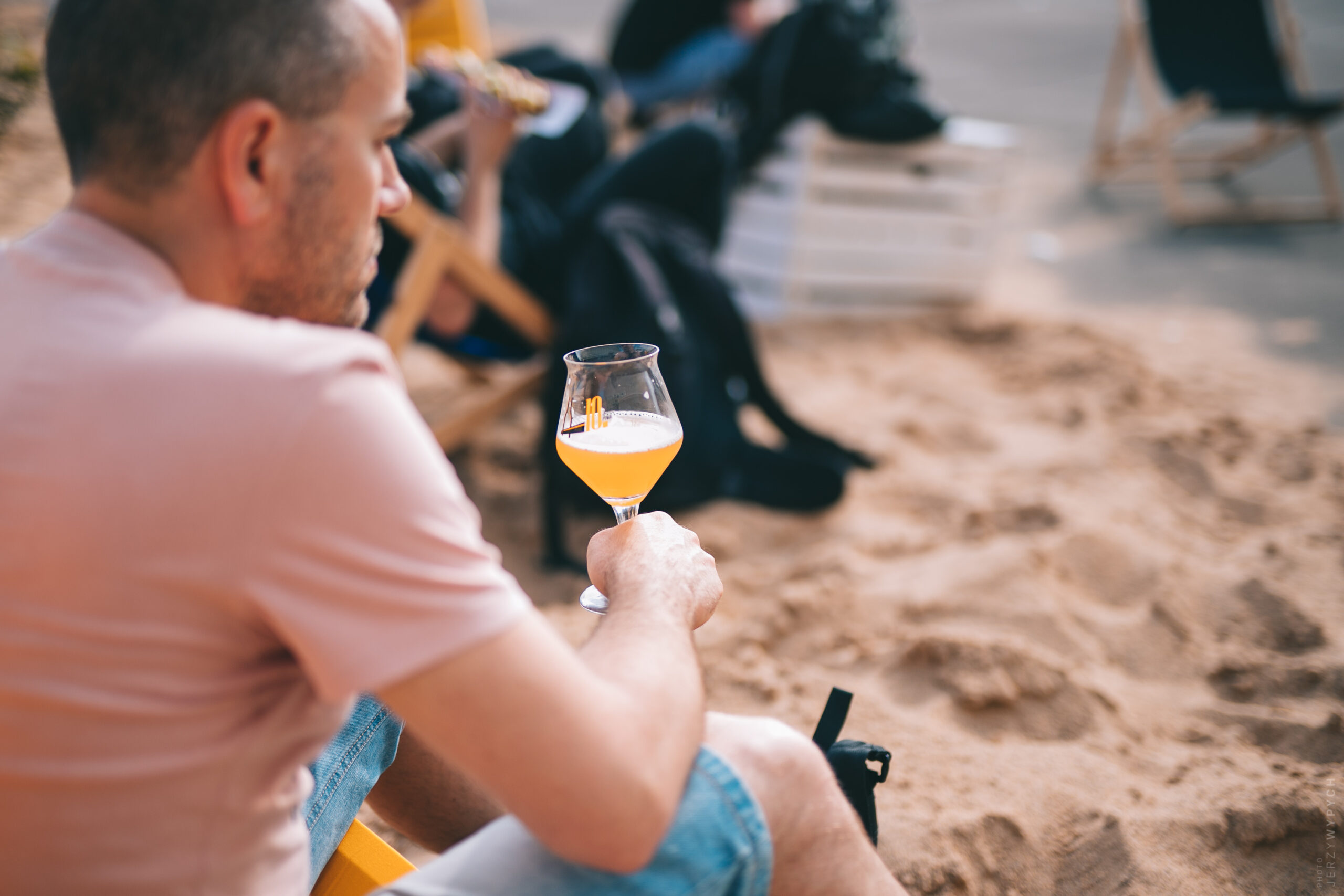 Zdjęcie z festiwalu, mężczyzna z kielichem piwa siedzi na plaży festiwalowej
